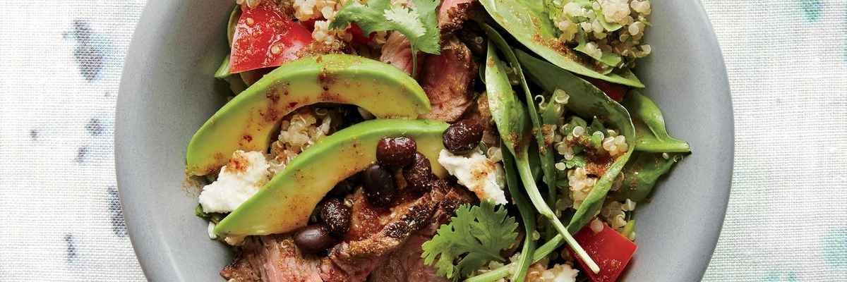 A blue bowl with beef strips, spinach, quinoa, tomatoes and spices.