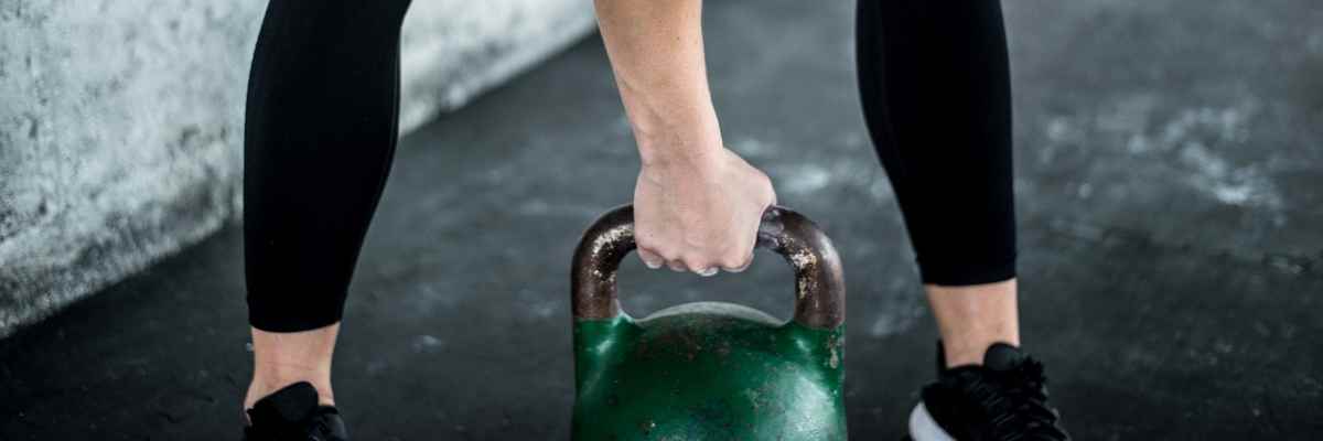 A person bending over and holding a green kettle bell with one hand. 